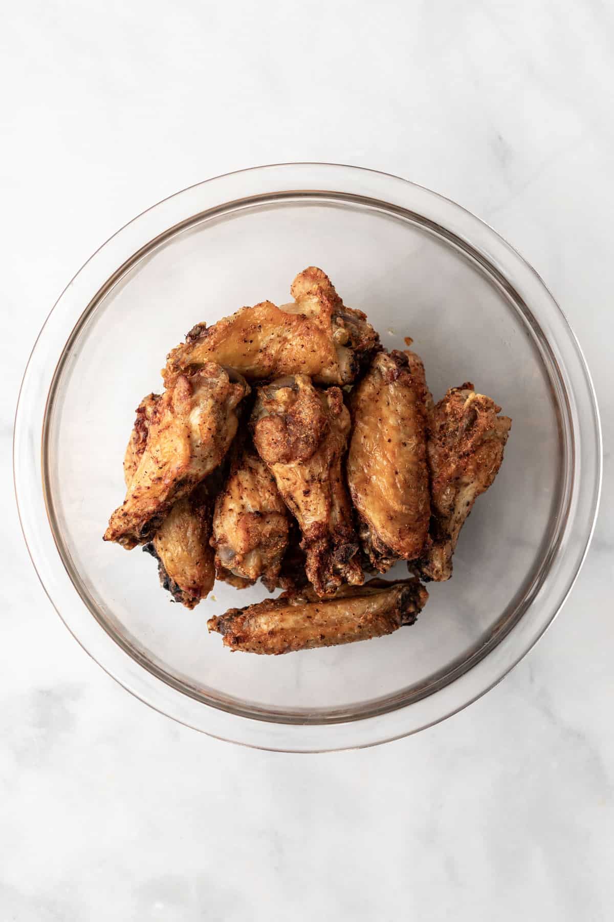 Cooked, golden brown chicken wings in a glass bowl.