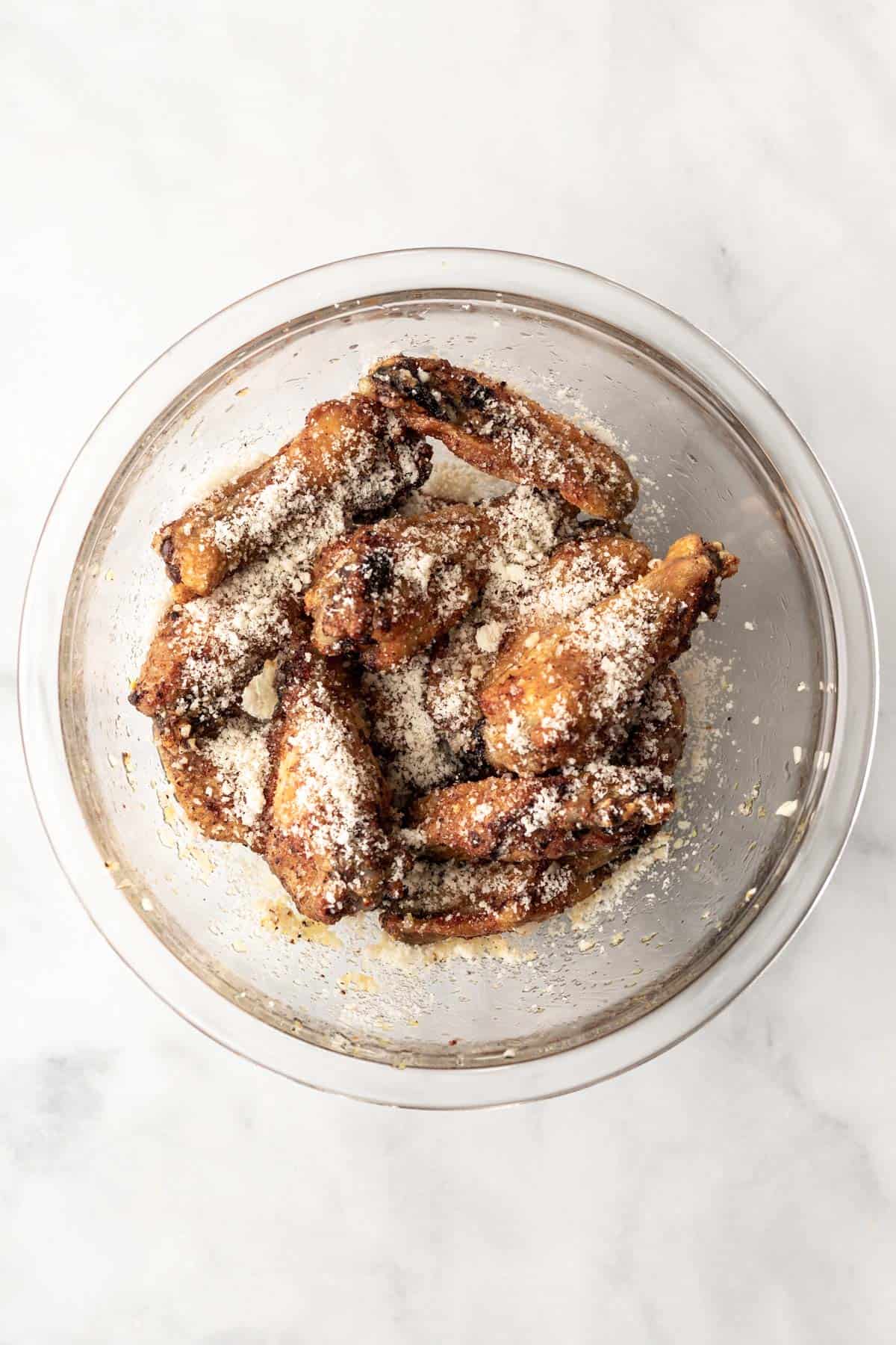 Air fryer chicken wings in a glass bowl with a sprinkle of parmesan cheese on top.