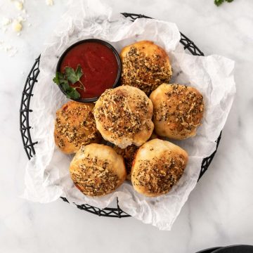 Air fryer pizza rolls piled into a black wire basket with a side of marinara sauce for dipping.