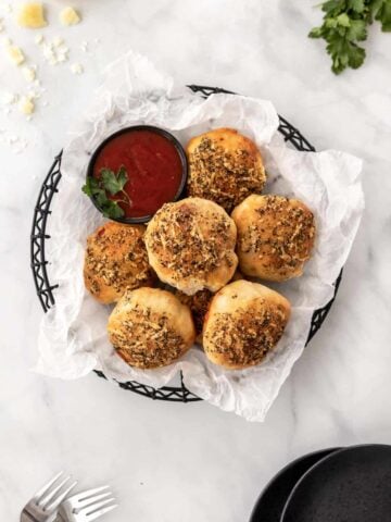 Air fryer pizza rolls piled into a black wire basket with a side of marinara sauce for dipping.