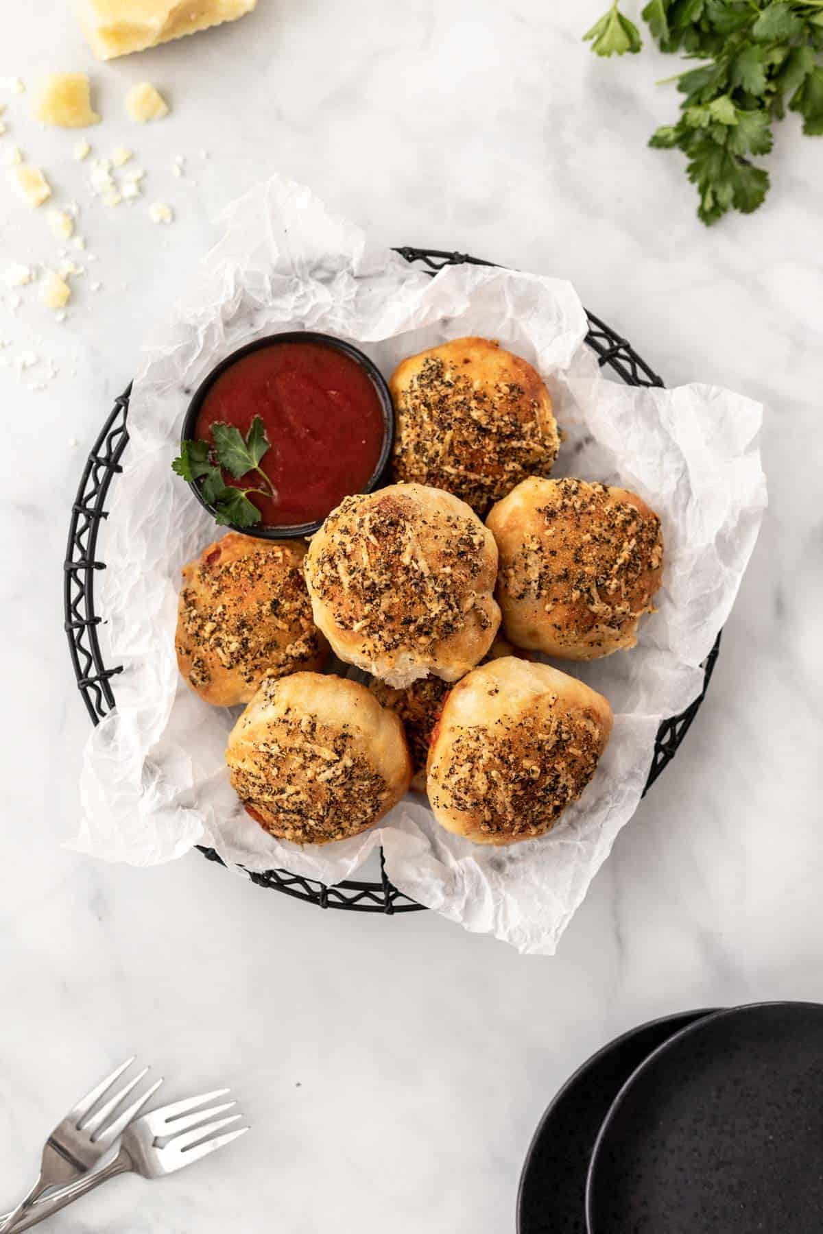 Air fryer pizza rolls piled into a black wire basket with a side of marinara sauce for dipping.