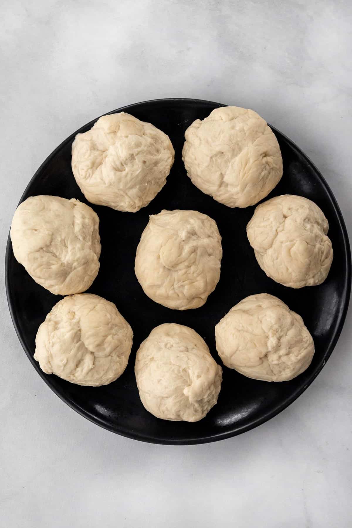 Pizza dough separated into 8 balls on a dark plate.