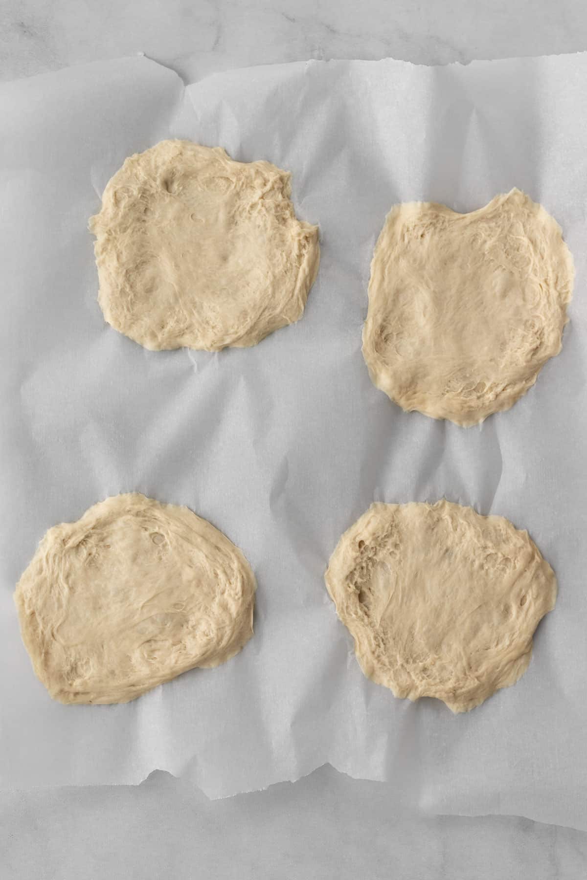 4 flattened balls of dough on a piece of parchment paper.