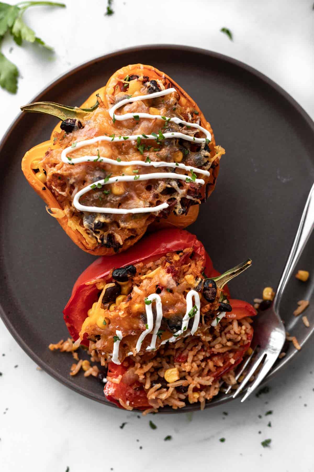 2 air fryer stuffed peppers drizzled with sour cream on a gray plate with a fork and filling pouring out.