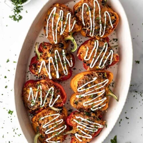 Air fryer stuffed peppers garnished with sour cream and parsley in a large oval serving bowl.