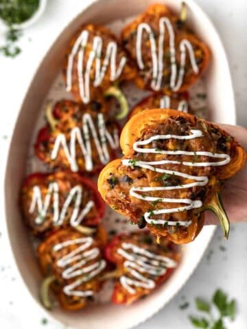 Multiple air fryer stuffed peppers drizzled with sour cream in an oval dish with one pepper raised higher to show detail.