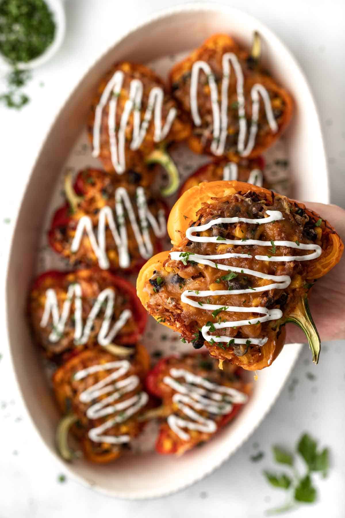 Multiple air fryer stuffed peppers drizzled with sour cream in an oval dish with one pepper raised higher to show detail.