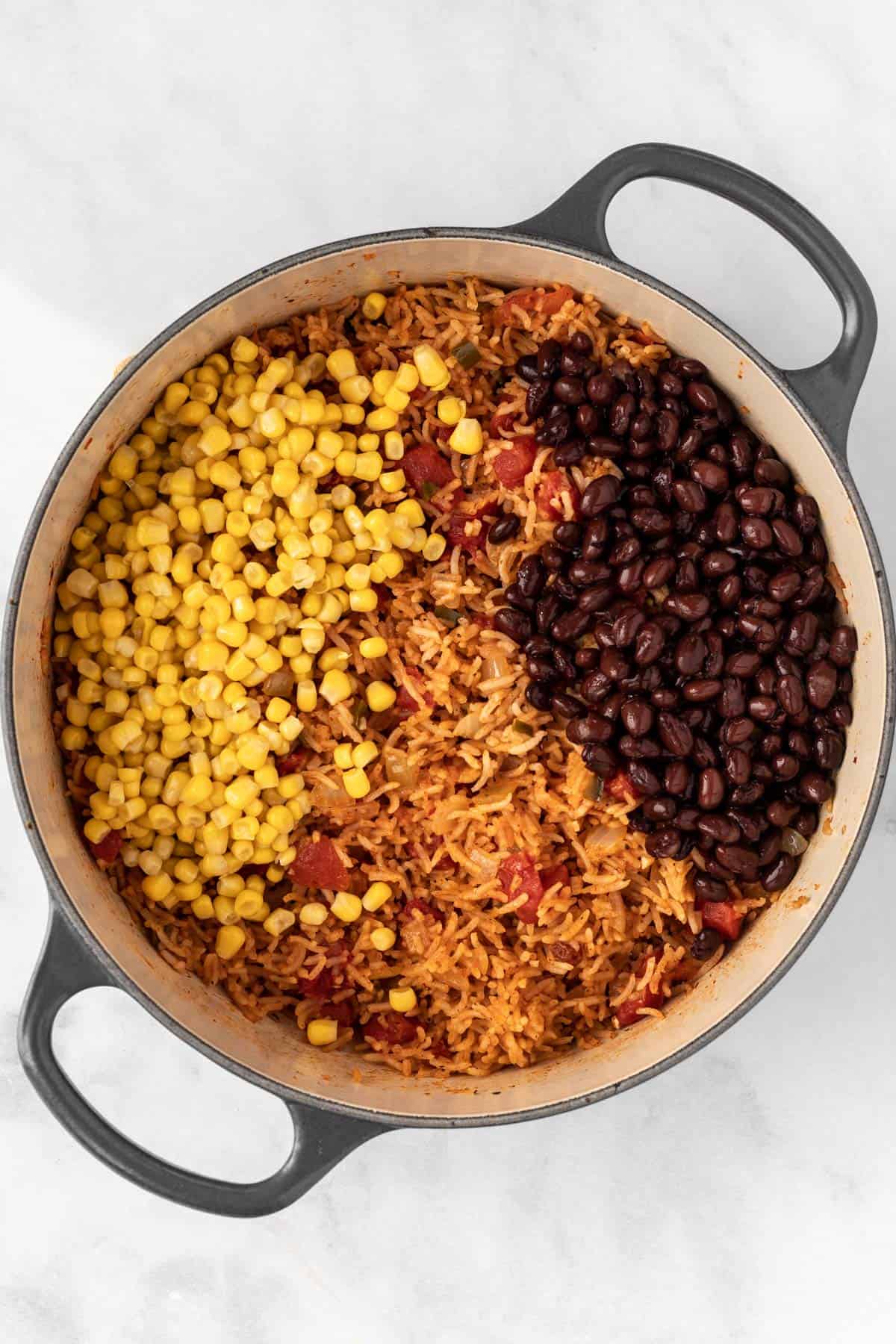 Cooked rice mixture in a dutch oven with corn and black beans on top.