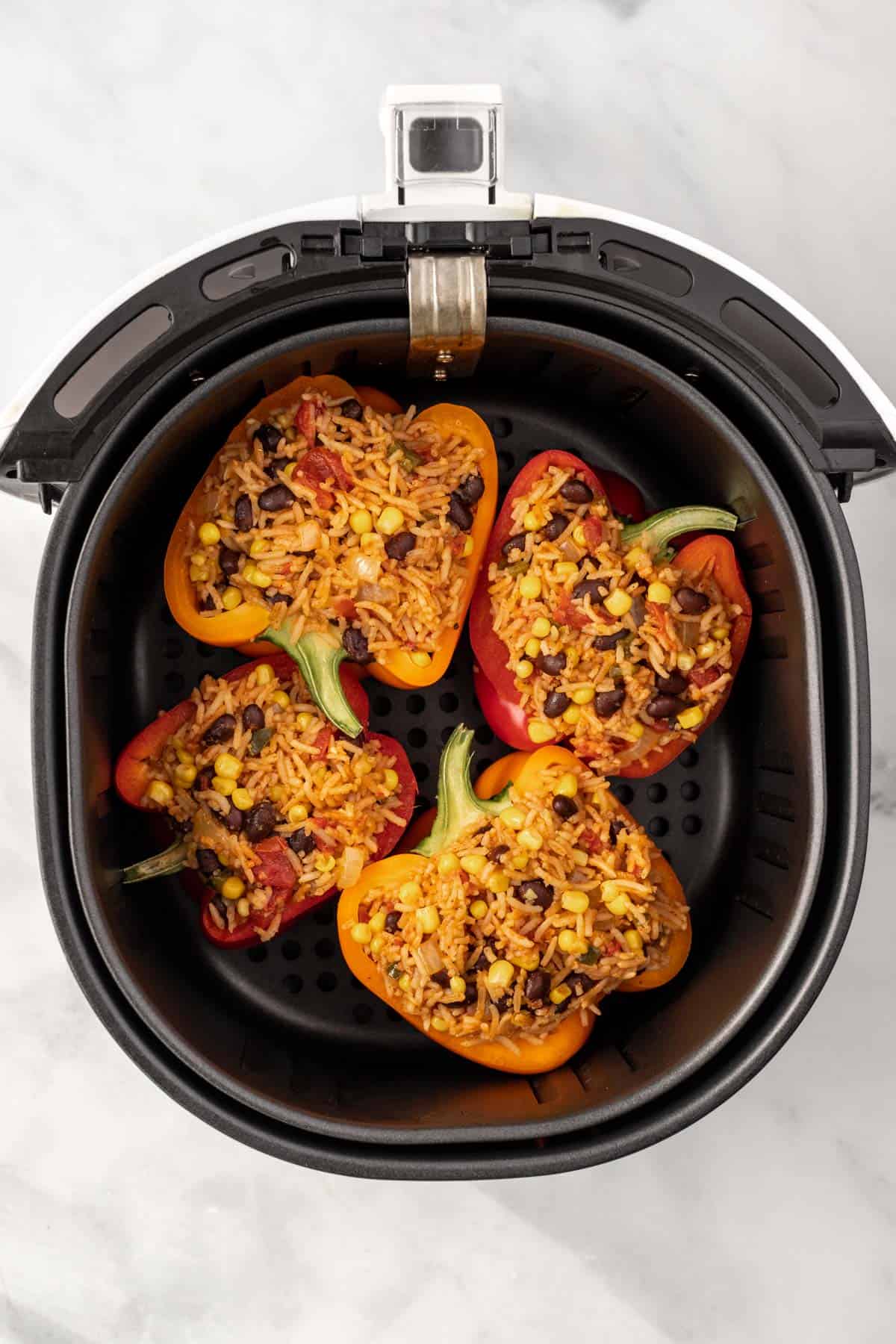 Uncooked stuffed peppers in an air fryer basket.