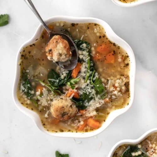 Instant pot italian wedding soup in 3 white bowls with parsley scattered around them.