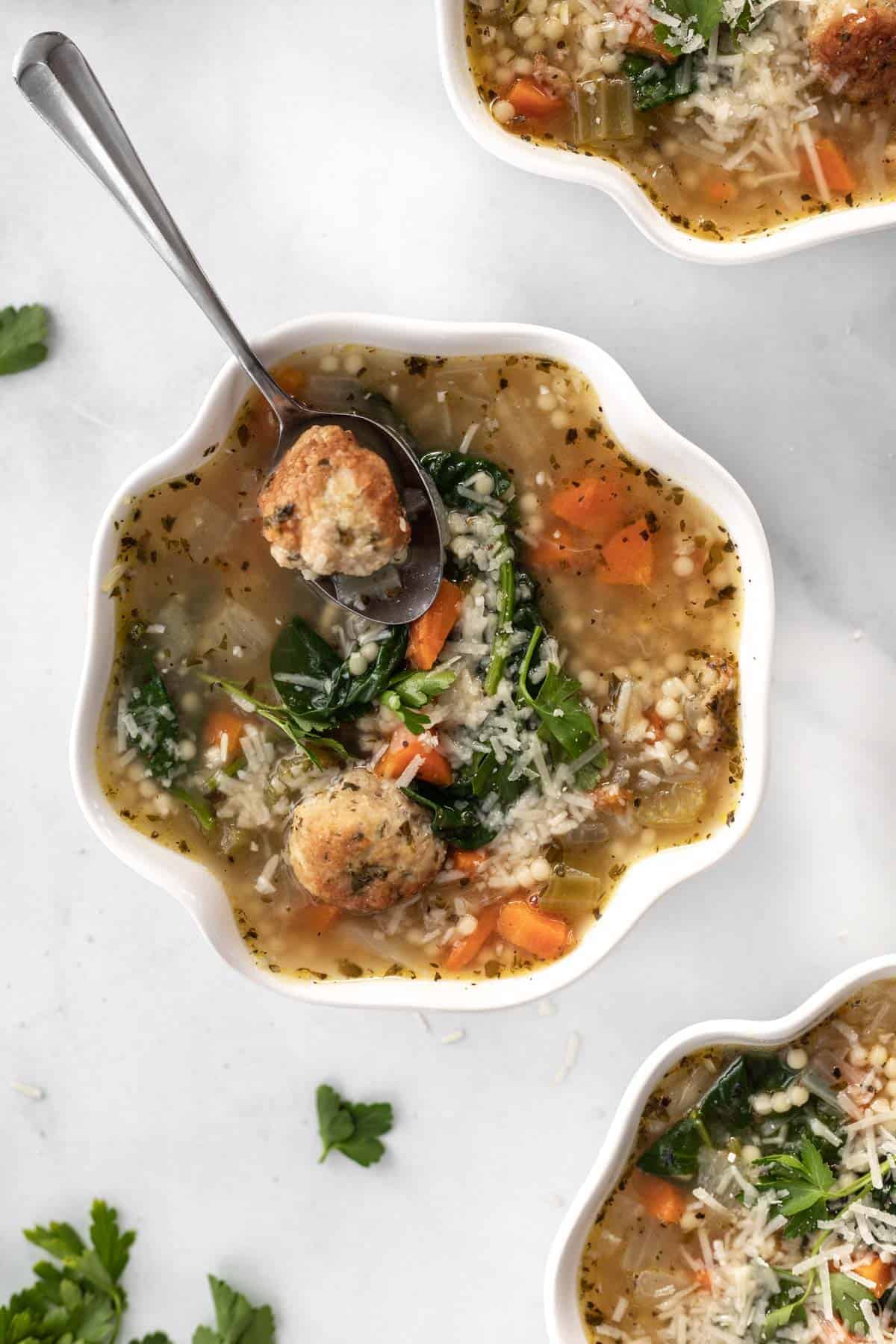 Instant pot italian wedding soup in 3 white bowls with parsley scattered around them.