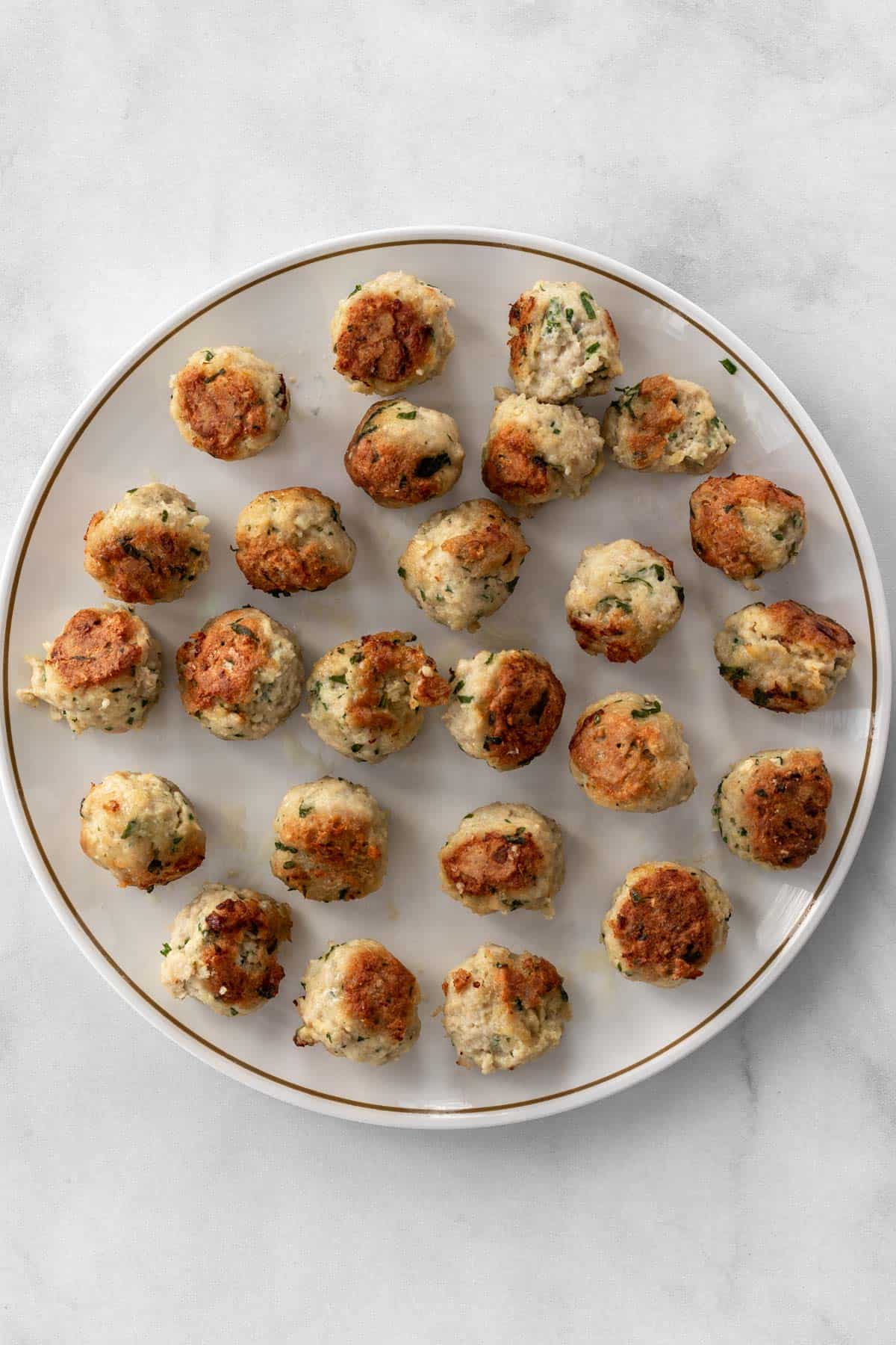 Perfectly golden brown meatballs on a white plate.