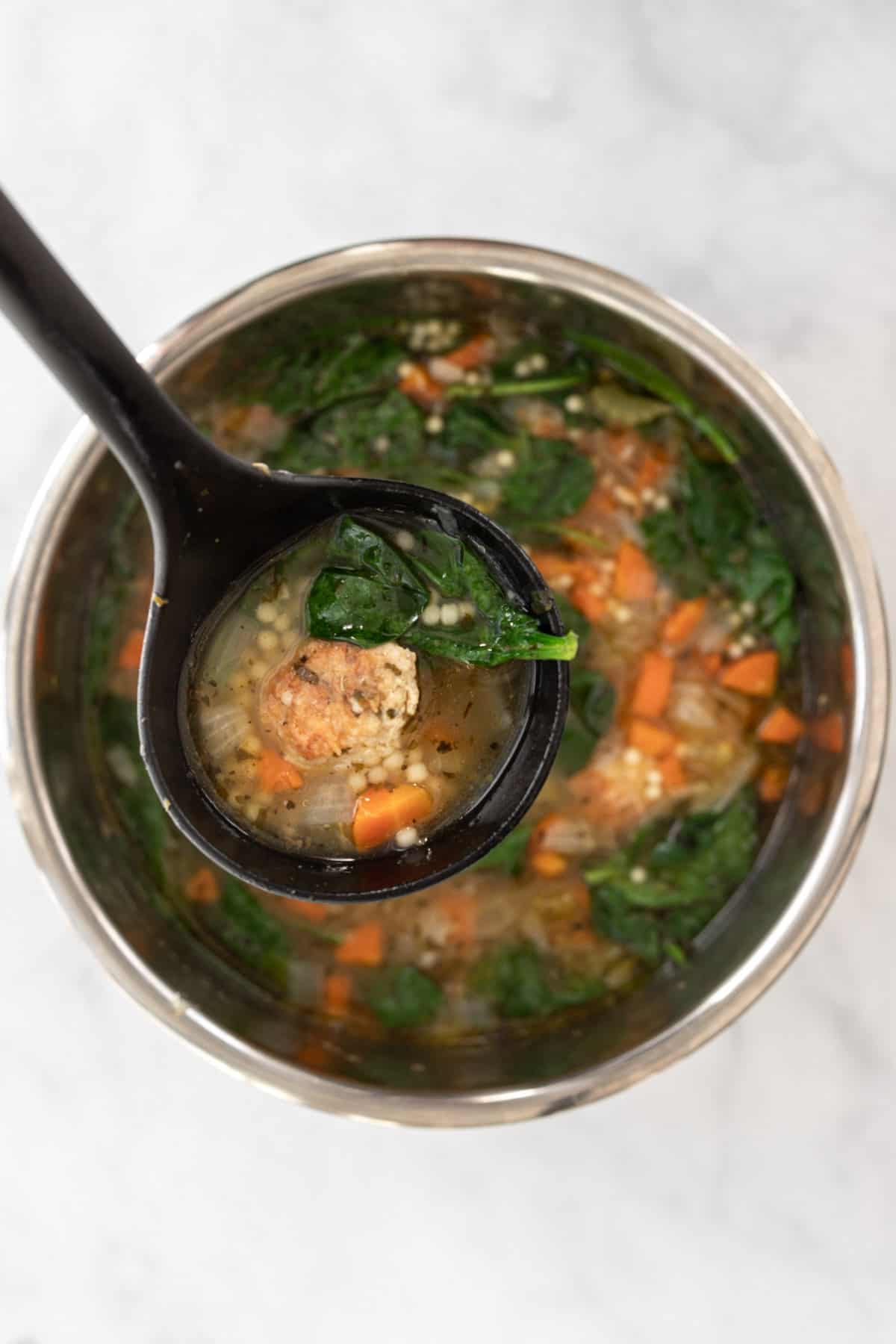 Italian wedding soup in a black ladle hovering over the pot of an instant pot.