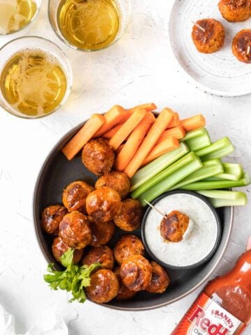 Buffalo turkey meatballs in a serving dish with a side of ranch, celery, and carrot sticks.