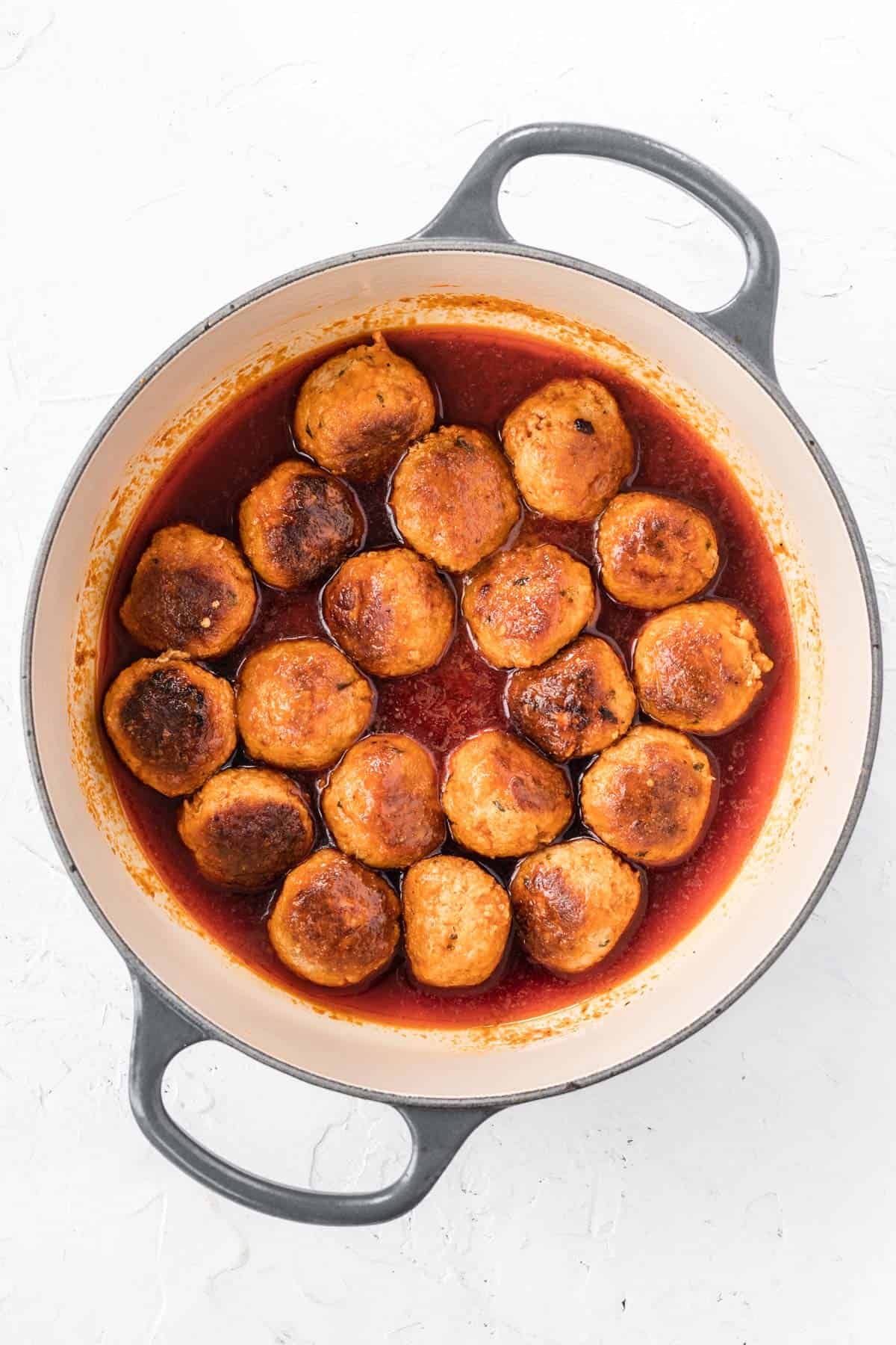 Turkey meatballs in buffalo sauce inside a dutch oven.