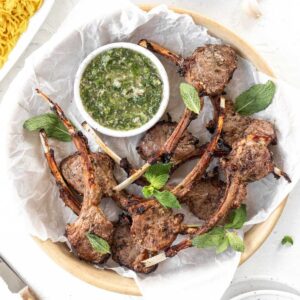 Air fryer lamb chops in a serving dish with a side of chimichurri.