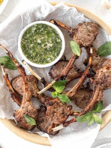 Air fryer lamb chops in a serving dish with a side of chimichurri.