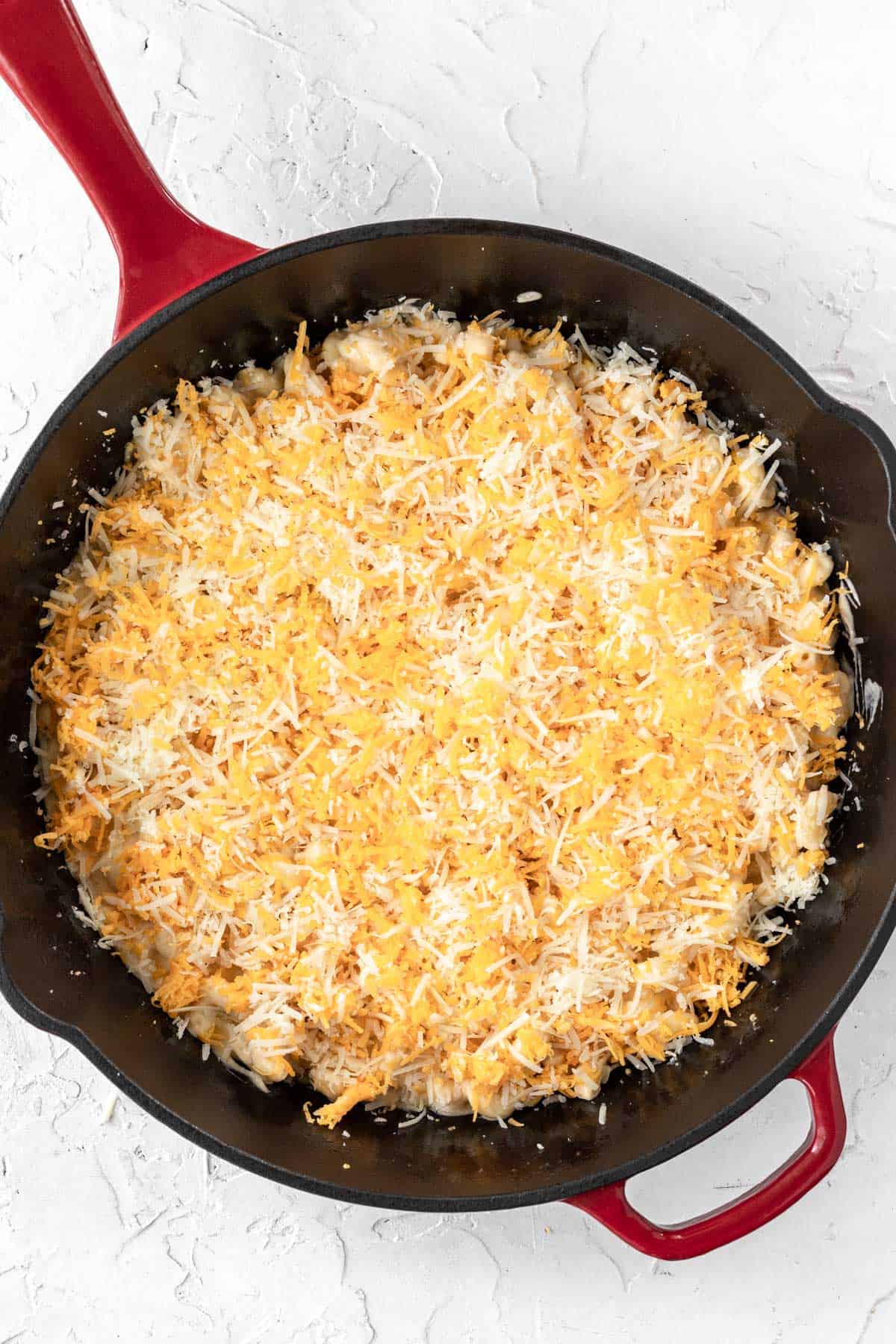 Pasta noodles covered in cheese sauce layered with more freshly grated cheese in a large cast iron skillet.