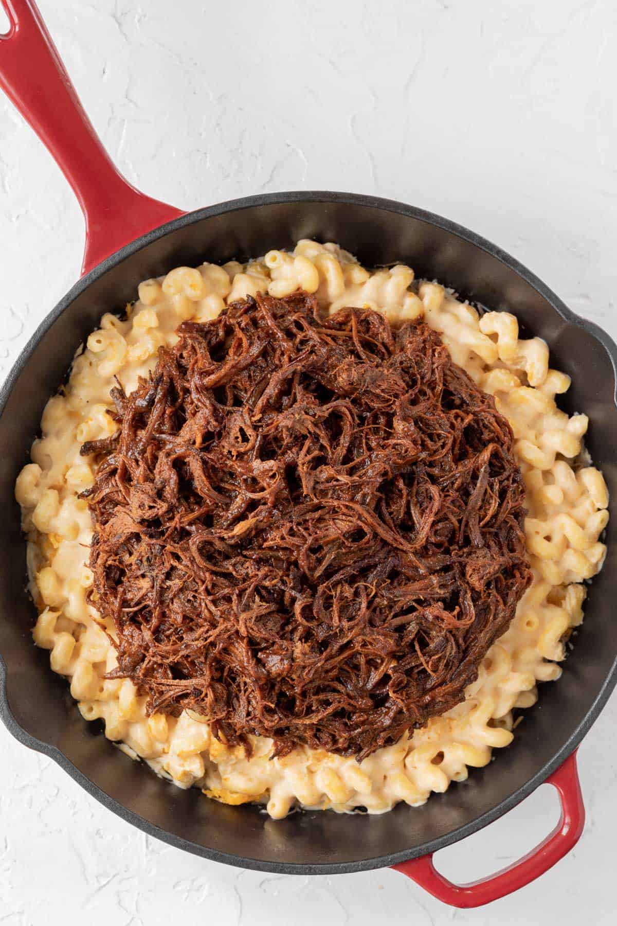 Pre-baked creamy mac and cheese in a large cast iron skillet topped with shredded BBQ brisket. 