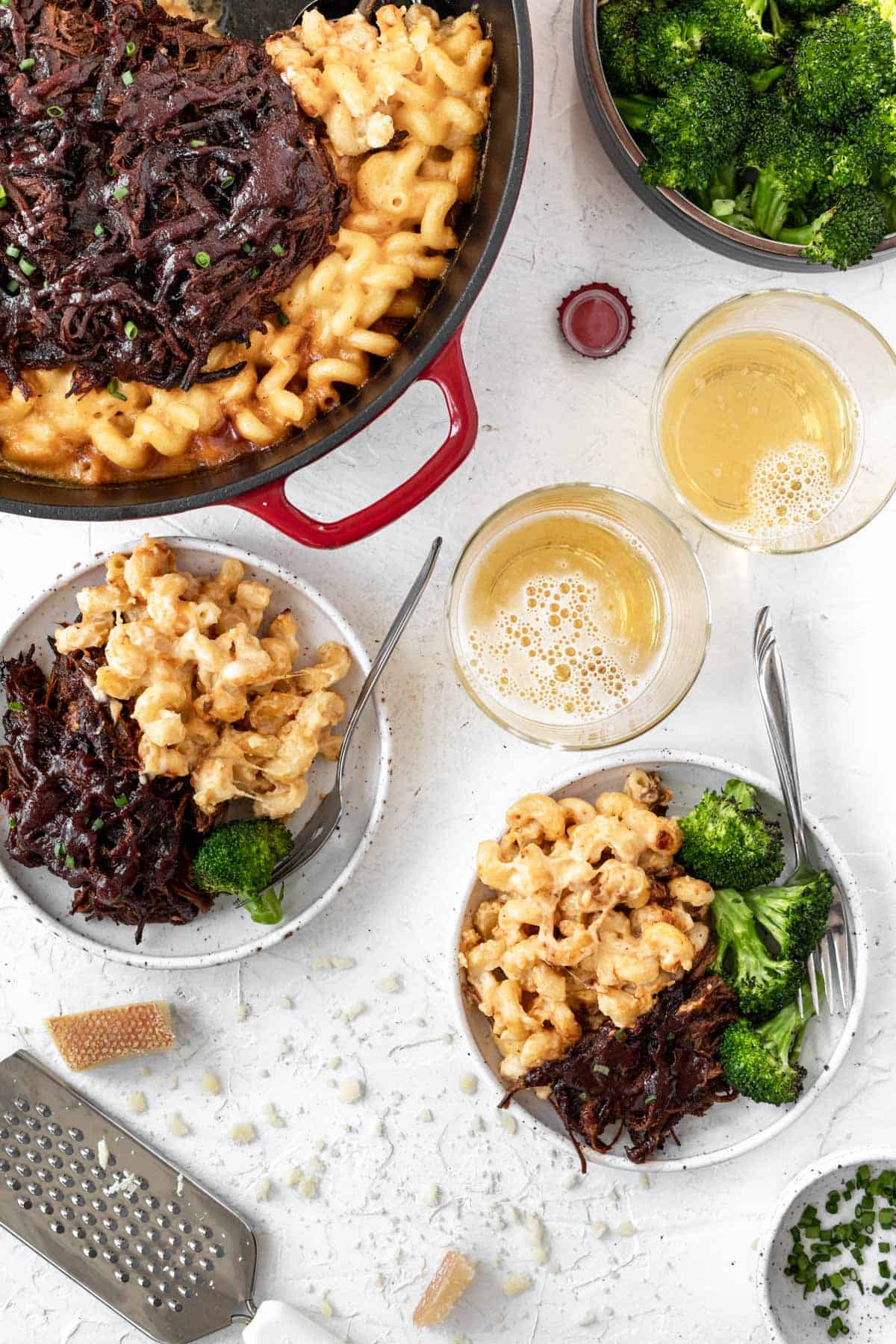 Creamy cheddar baked brisket mac and cheese served on two small plates with a side of broccoli and two glasses of beer.