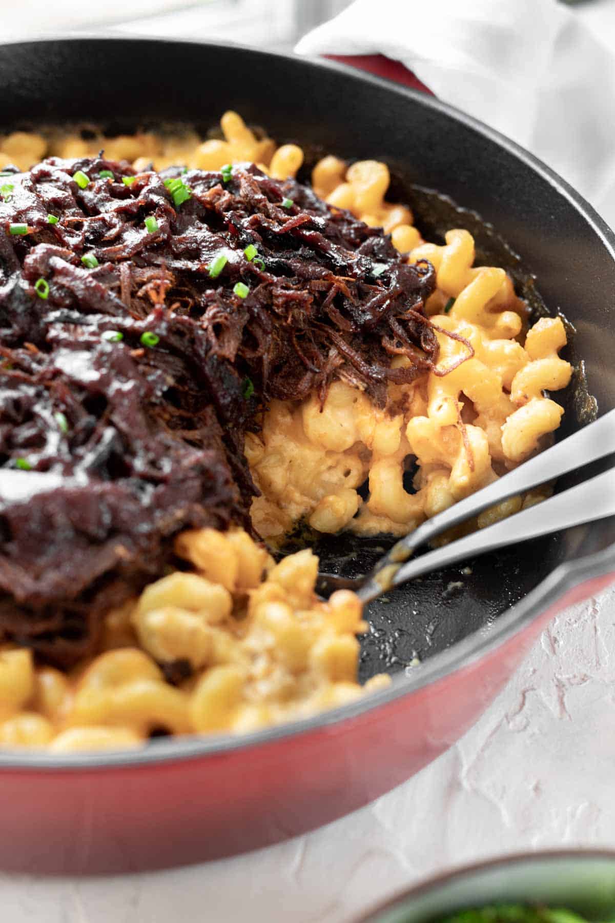 A closeup view of the cheesy noodles and the BBQ brisket in a cast iron skillet.