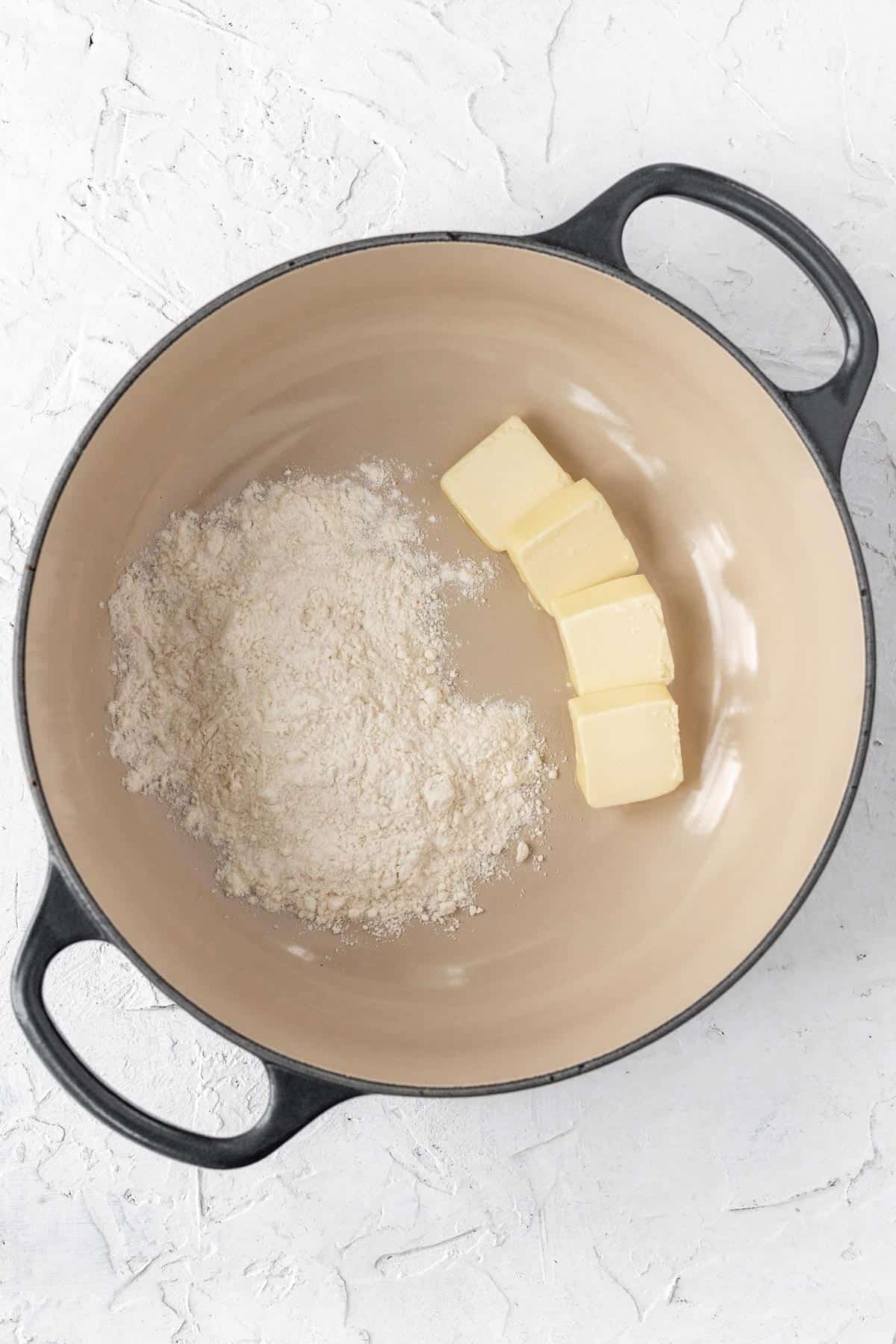 Slices of butter and a scoop of flour in the bottom of a dutch oven.