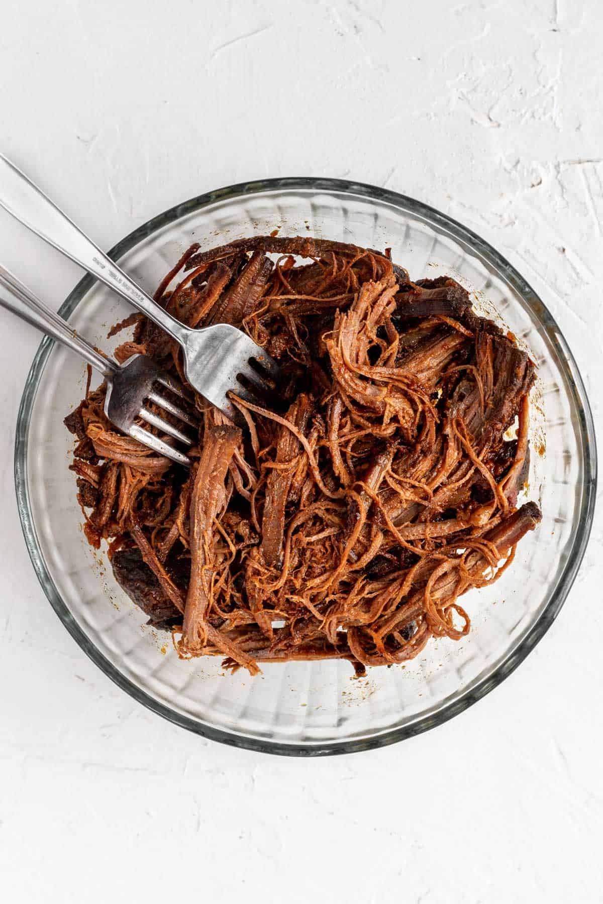 Brisket shredded in a glass bowl with 2 forks.