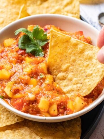 Mango habanero salsa in a bowl with a chip dipped in.