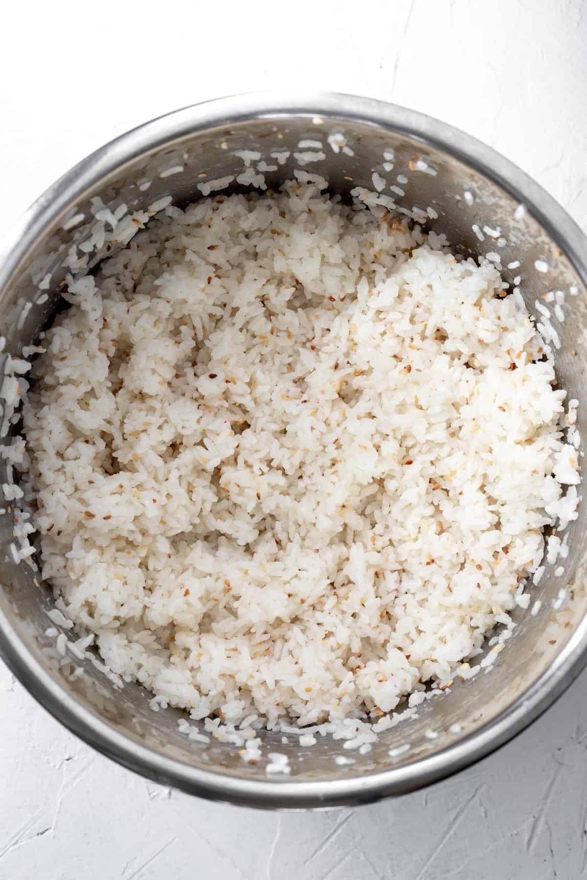 Cooked sushi rice mixed with vinegar and toasted sesame seeds in an instant pot.