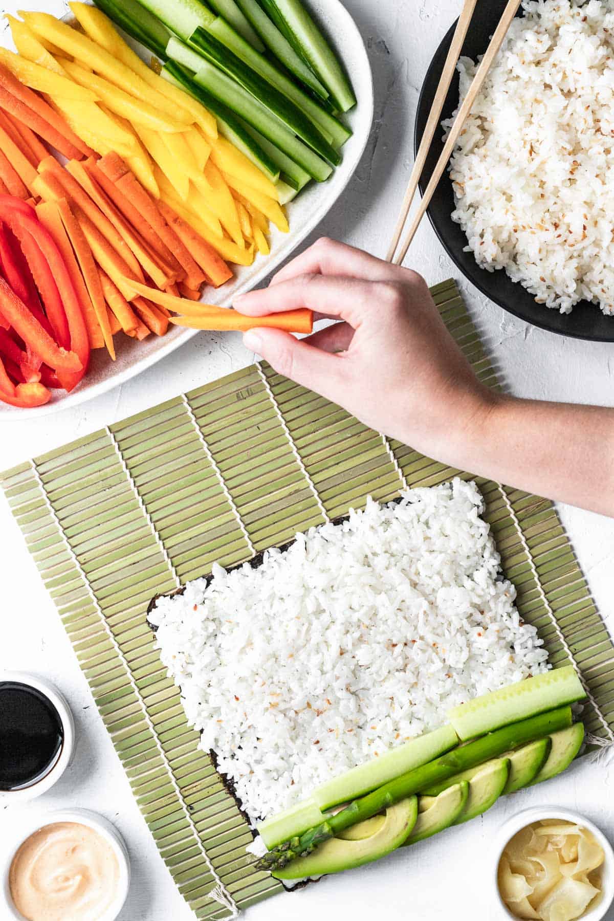 A hand grabbing sliced vegetables to place on top of sushi rice covered nori.