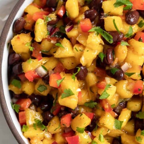 Close up view of mango salsa with black beans in a round serving dish.