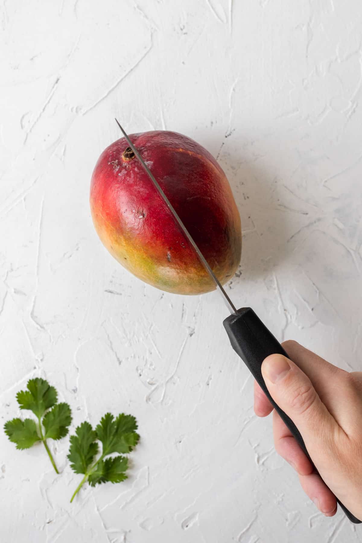 A knife cutting off one side of a mango.