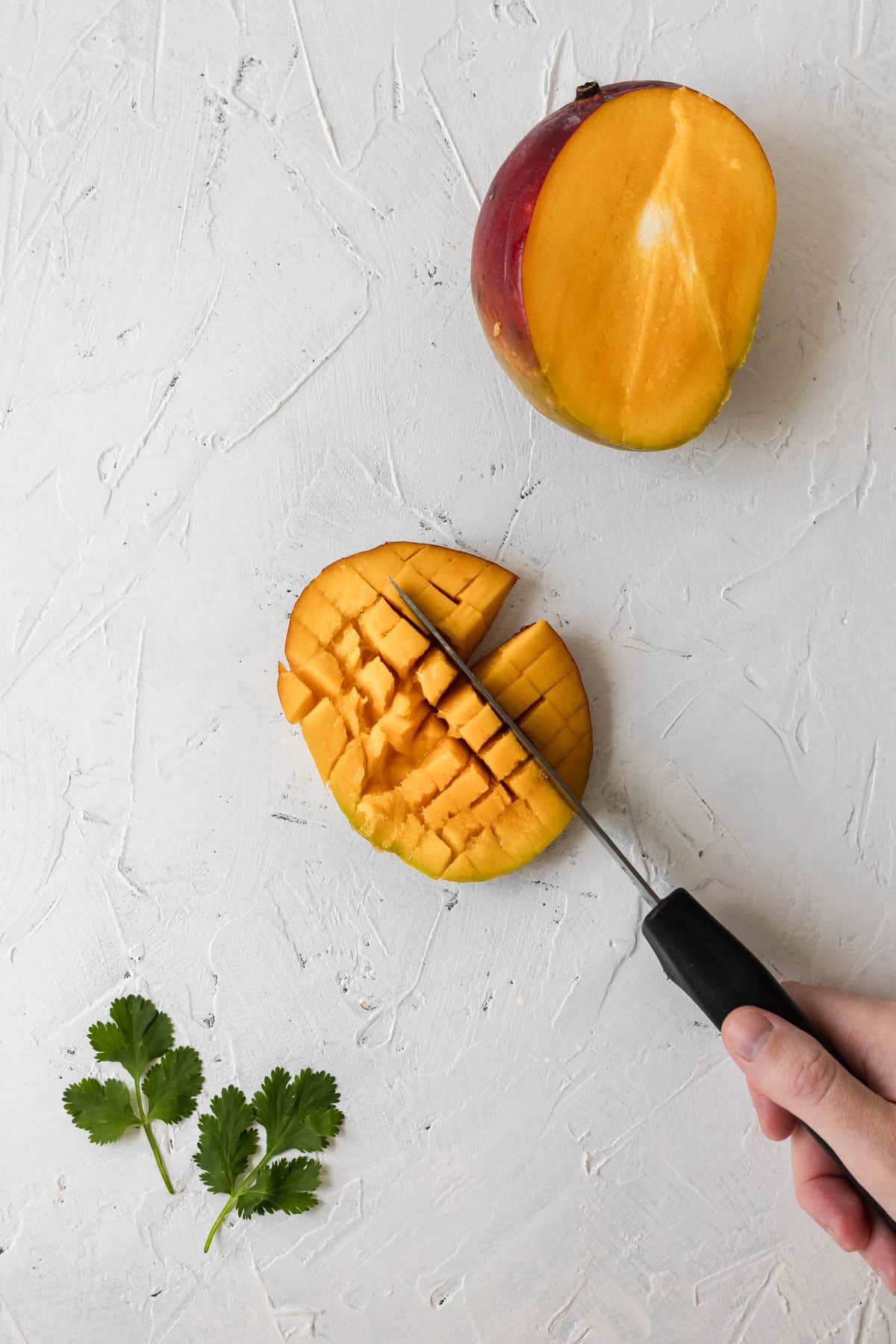 A knife cubing the inside of part of a mango.