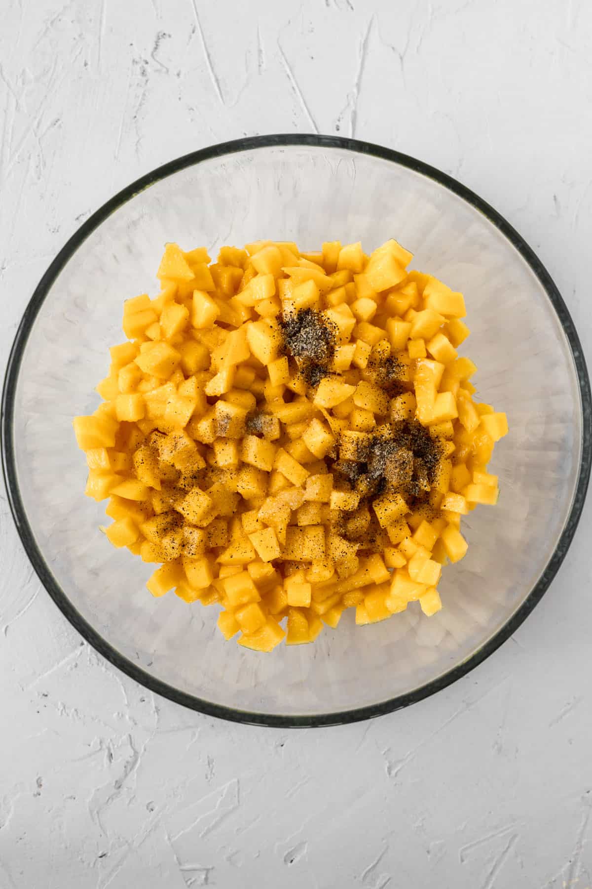 Cubed mango and seasonings in a glass bowl.