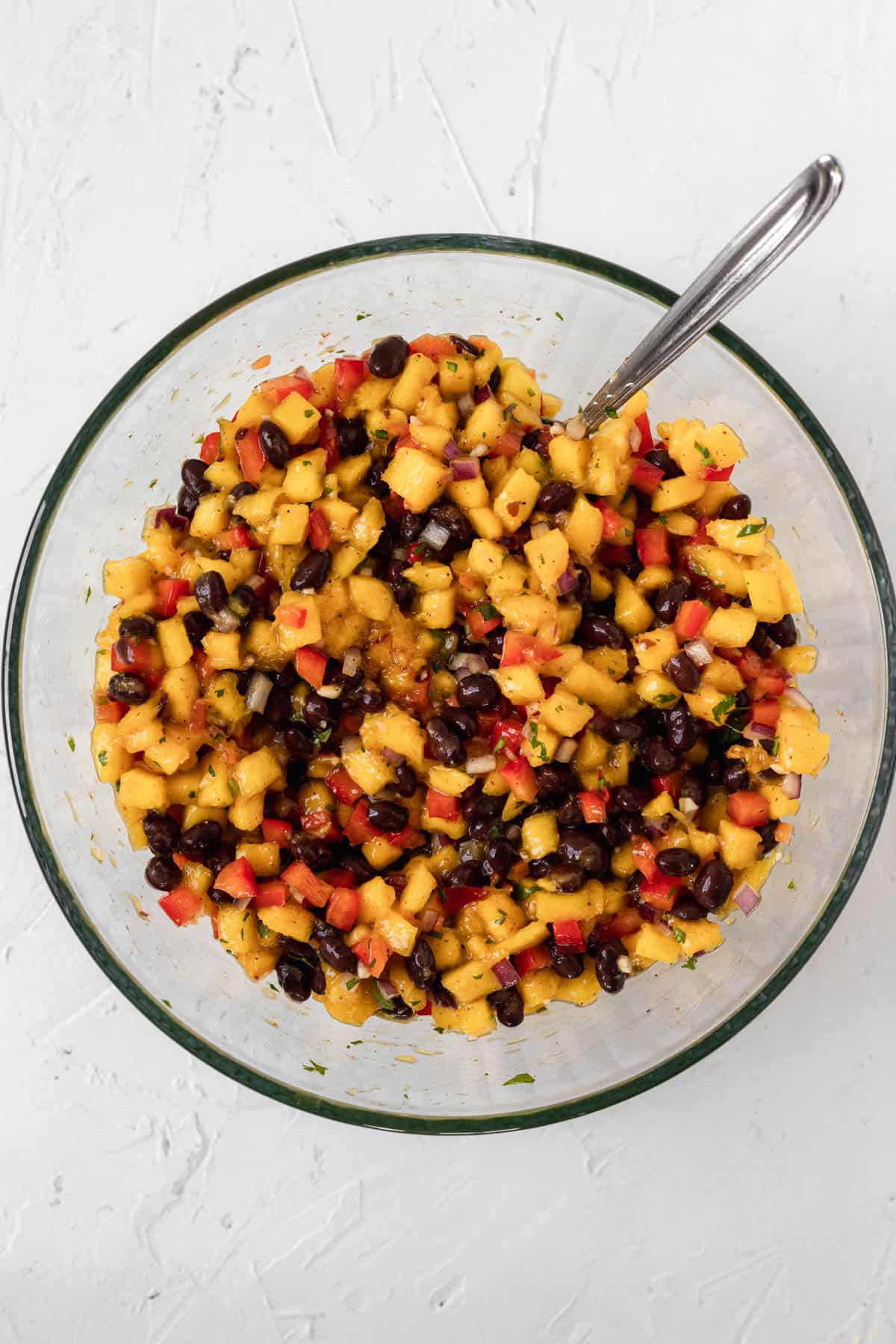 Fully mixed together mango habanero salsa with black beans in a glass bowl.