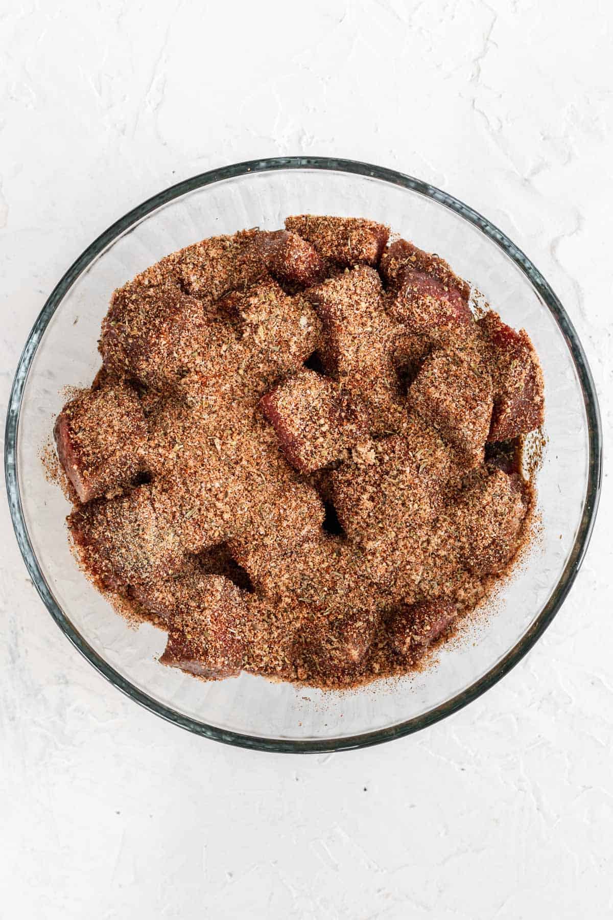 Seasoned raw cajun steak bites in a glass bowl.