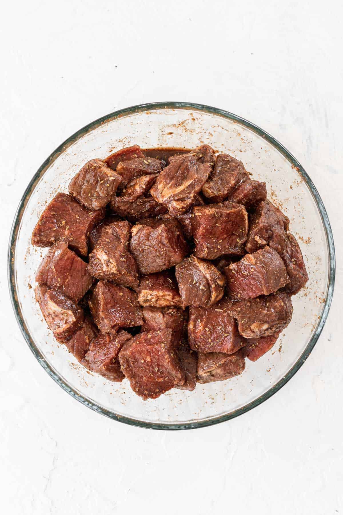 Cubed steak in a glass bowl topped with a balsamic marinade.