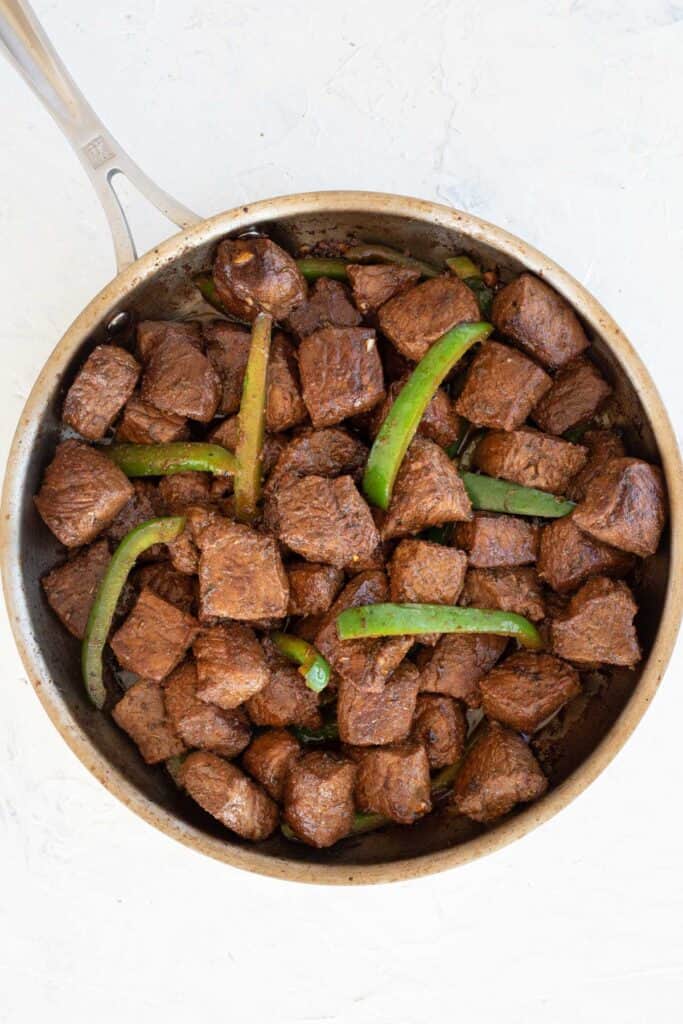 Steak bites with sauteed peppers in a skillet.