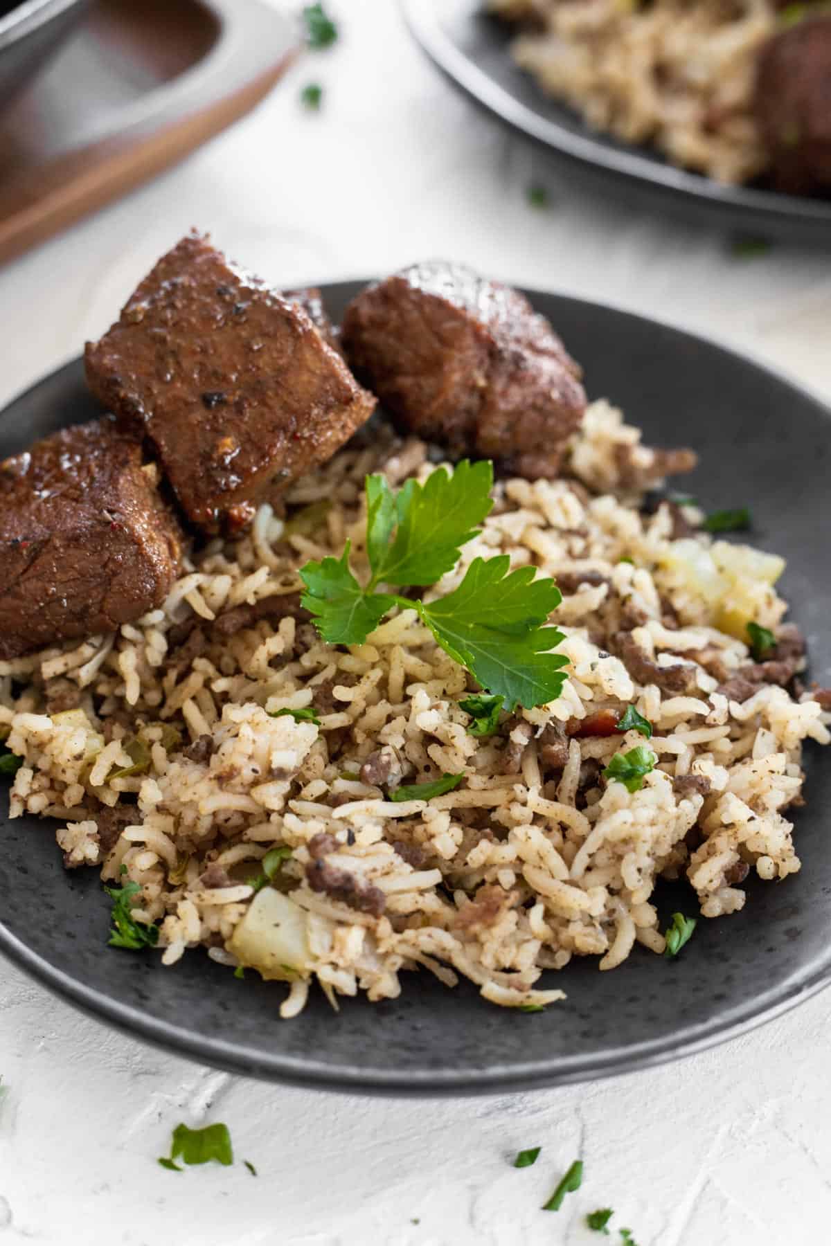 Beef and bacon dirty rice with a side of cajun steak bites on a black plate.