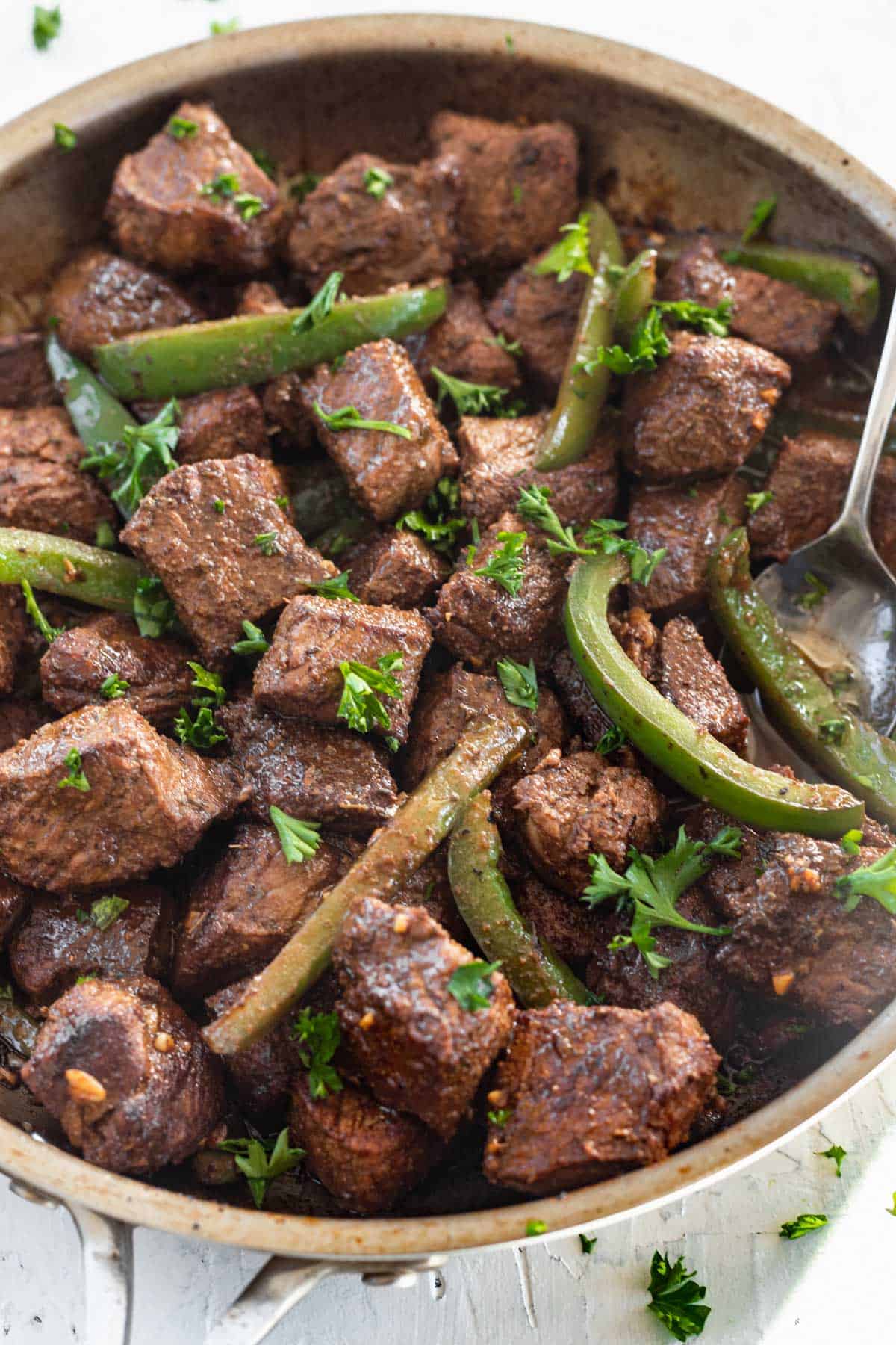 Cajun butter steak bites in a skillet with green bell peppers and parsley.