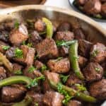 Balsamic marinated cajun steak bites with sauteed green peppers in a skillet.