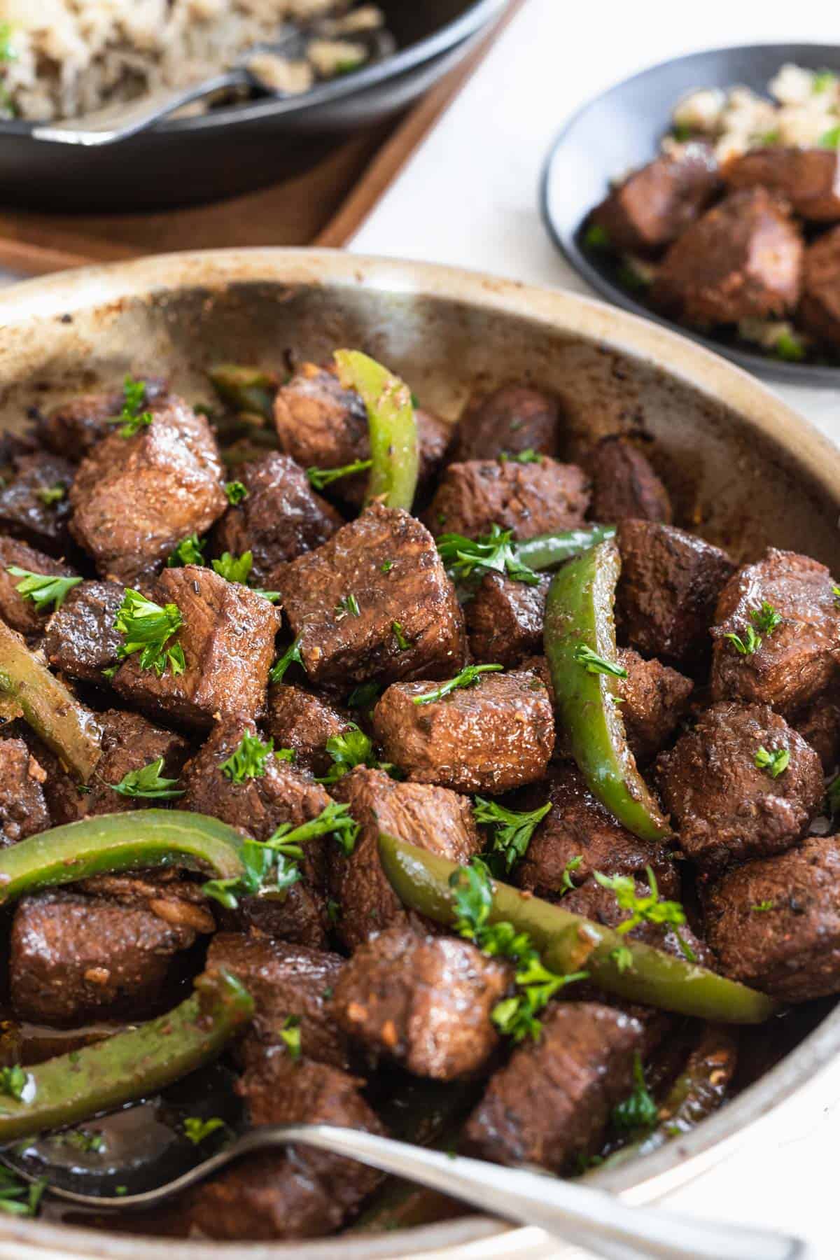 Balsamic marinated cajun steak bites with sauteed green peppers in a skillet.