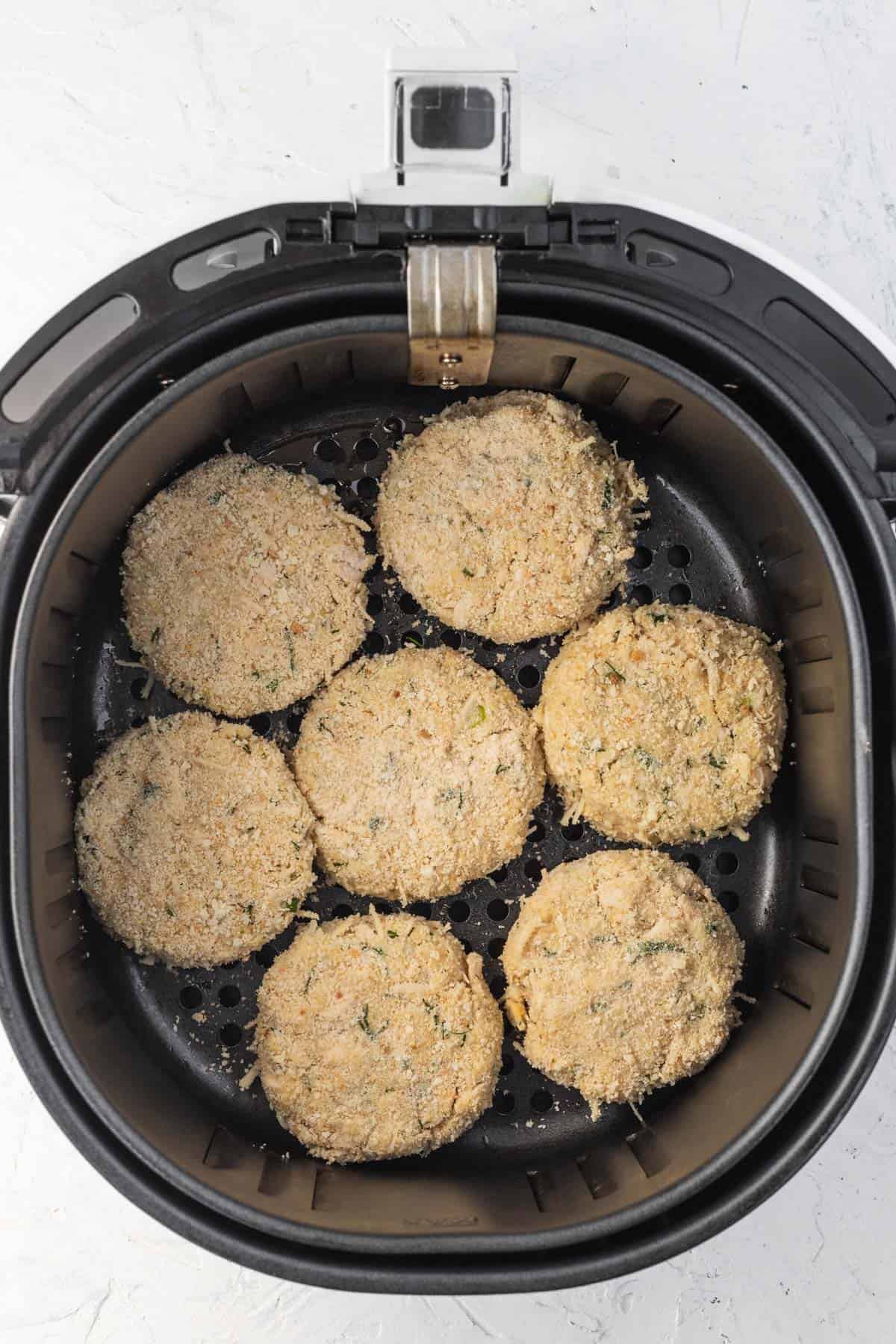 Formed uncooked chicken patties in a basket of an air fryer.