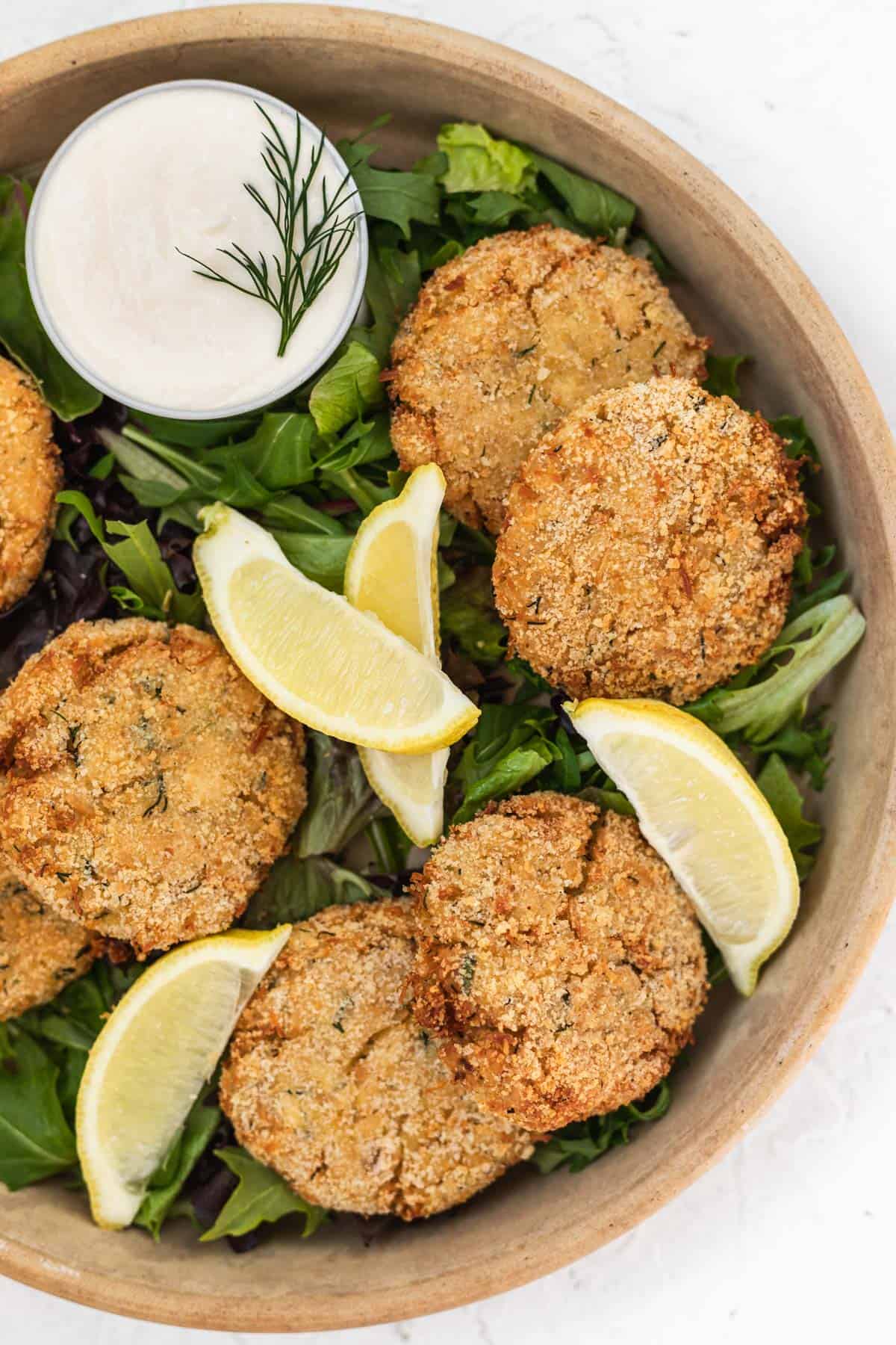 Chicken patties on a bed of lettuce in a large serving dish with lemon slices and a side of garlic aioli.