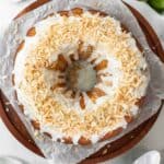 Coconut lime drizzle cake on a wooden cake stand with fresh limes around it.