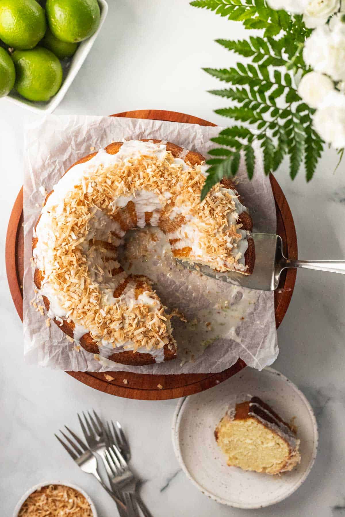 Coconut lime cake topped with toasted coconut with a slice removed.