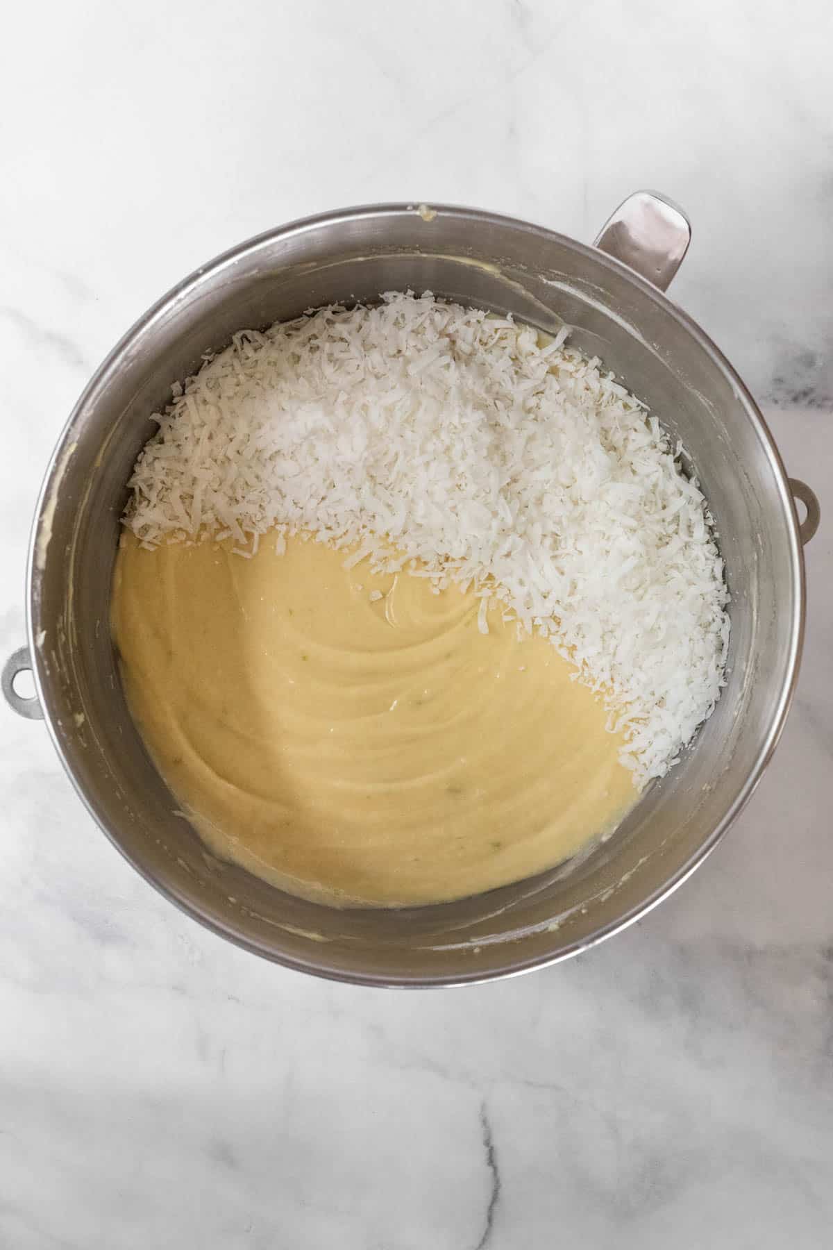 Coconut lime cake batter in a mixing bowl topped with sweetened coconut flakes.