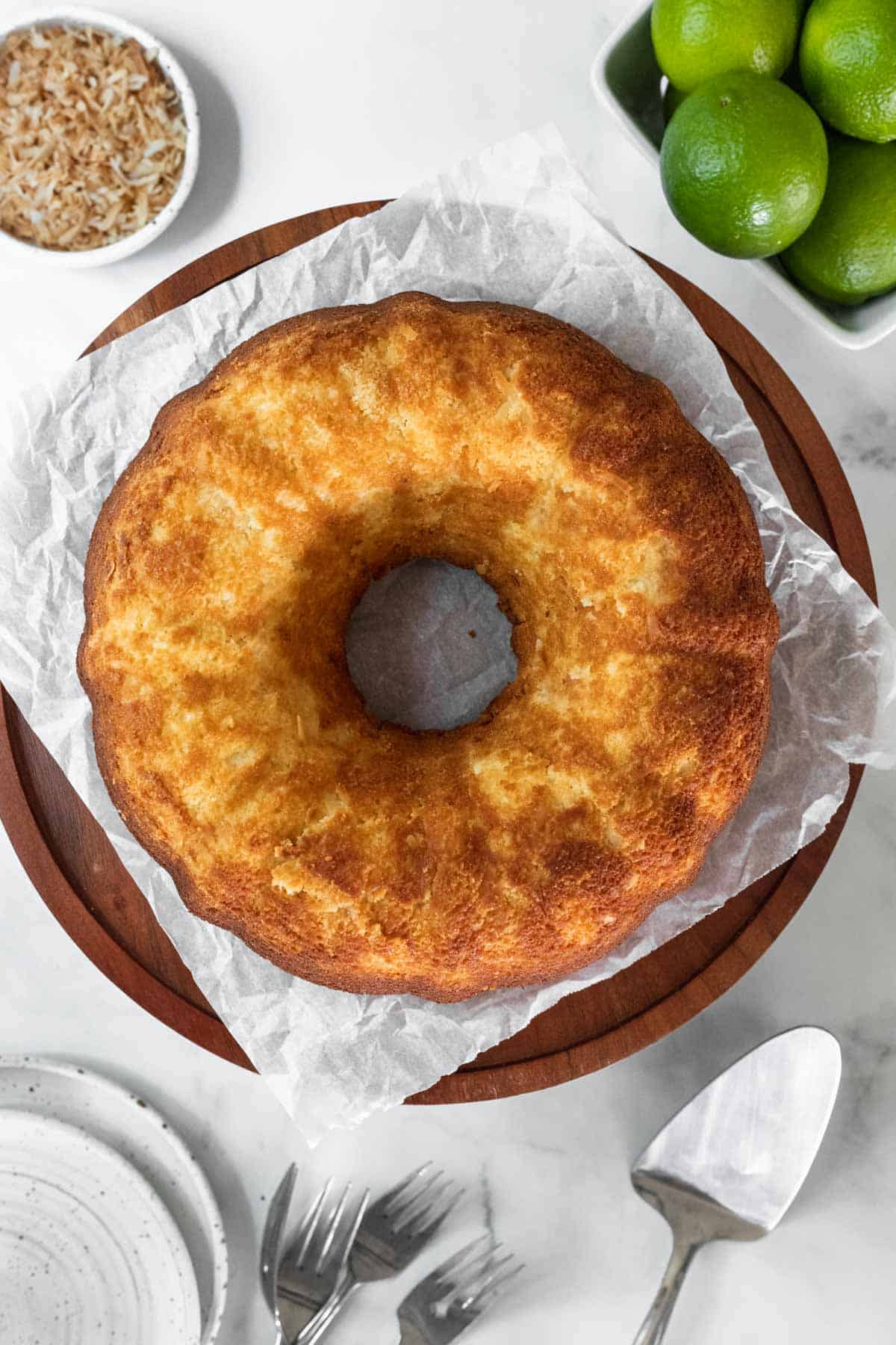 Baked coconut lime cake on a wooden cake stand ready to be drizzled.