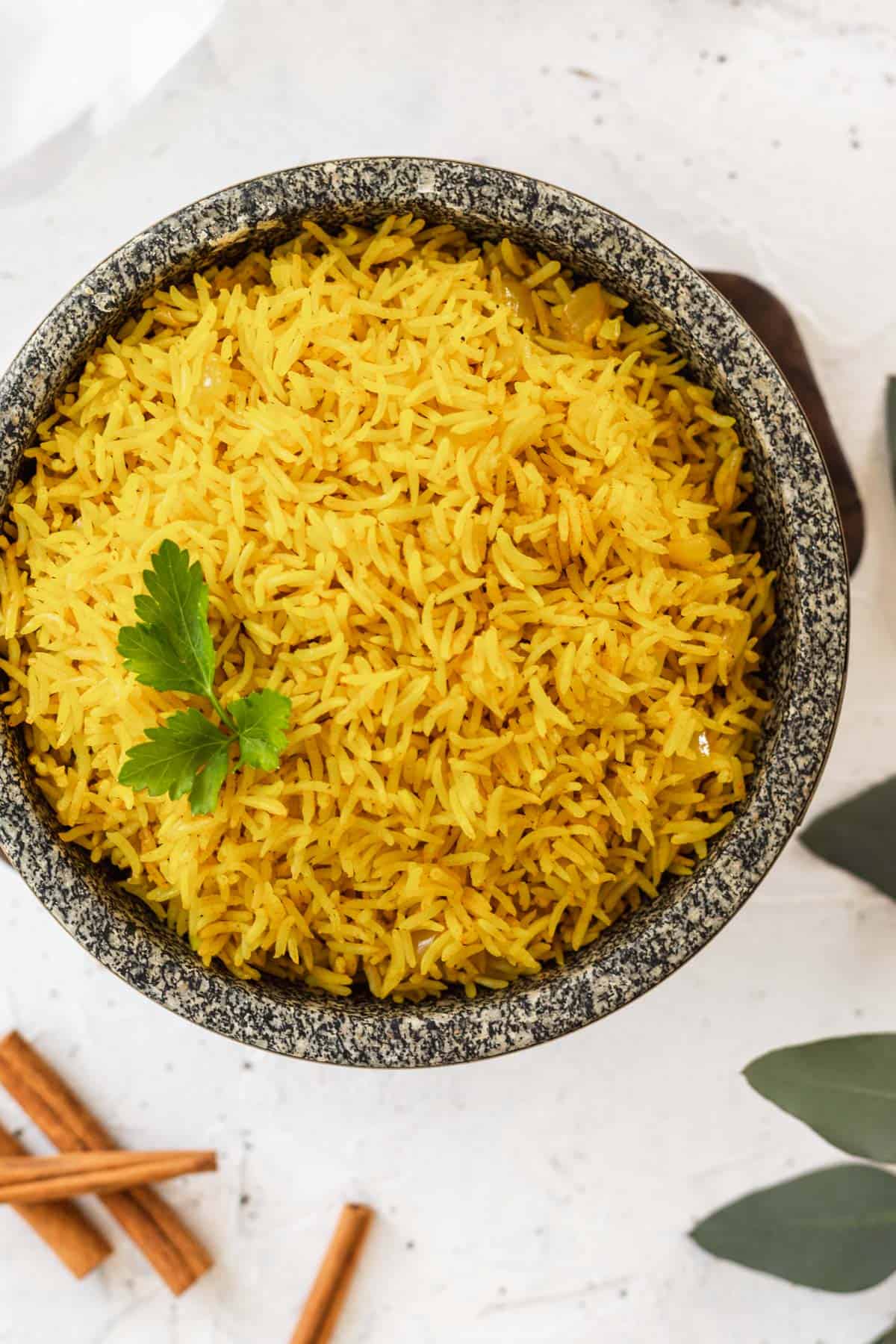 Fluffy homemade yellow rice in a stone bowl with cinnamon sticks and greenery off to the side.