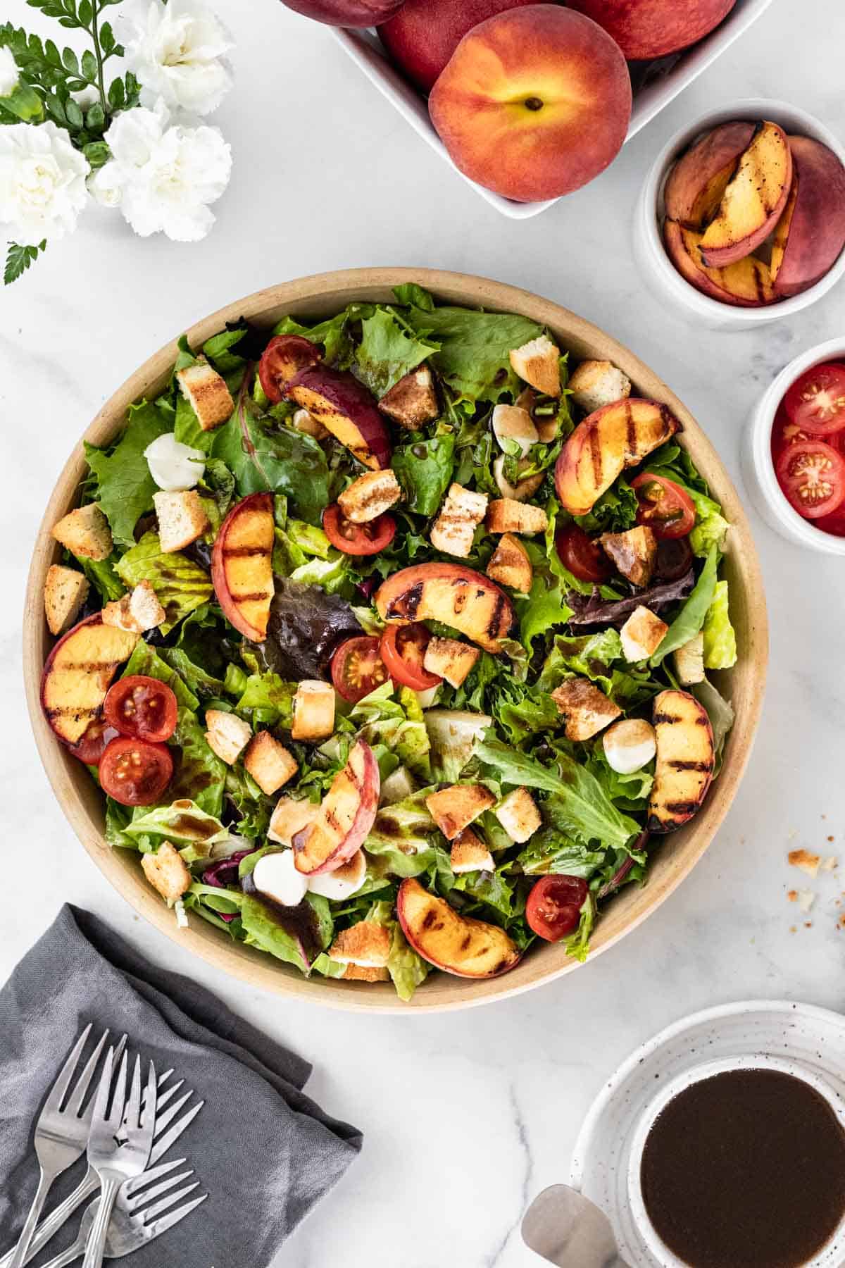 Assembled bruschetta salad with whole peaches, sliced peaches, sliced tomatoes, and balsamic dressing around it.